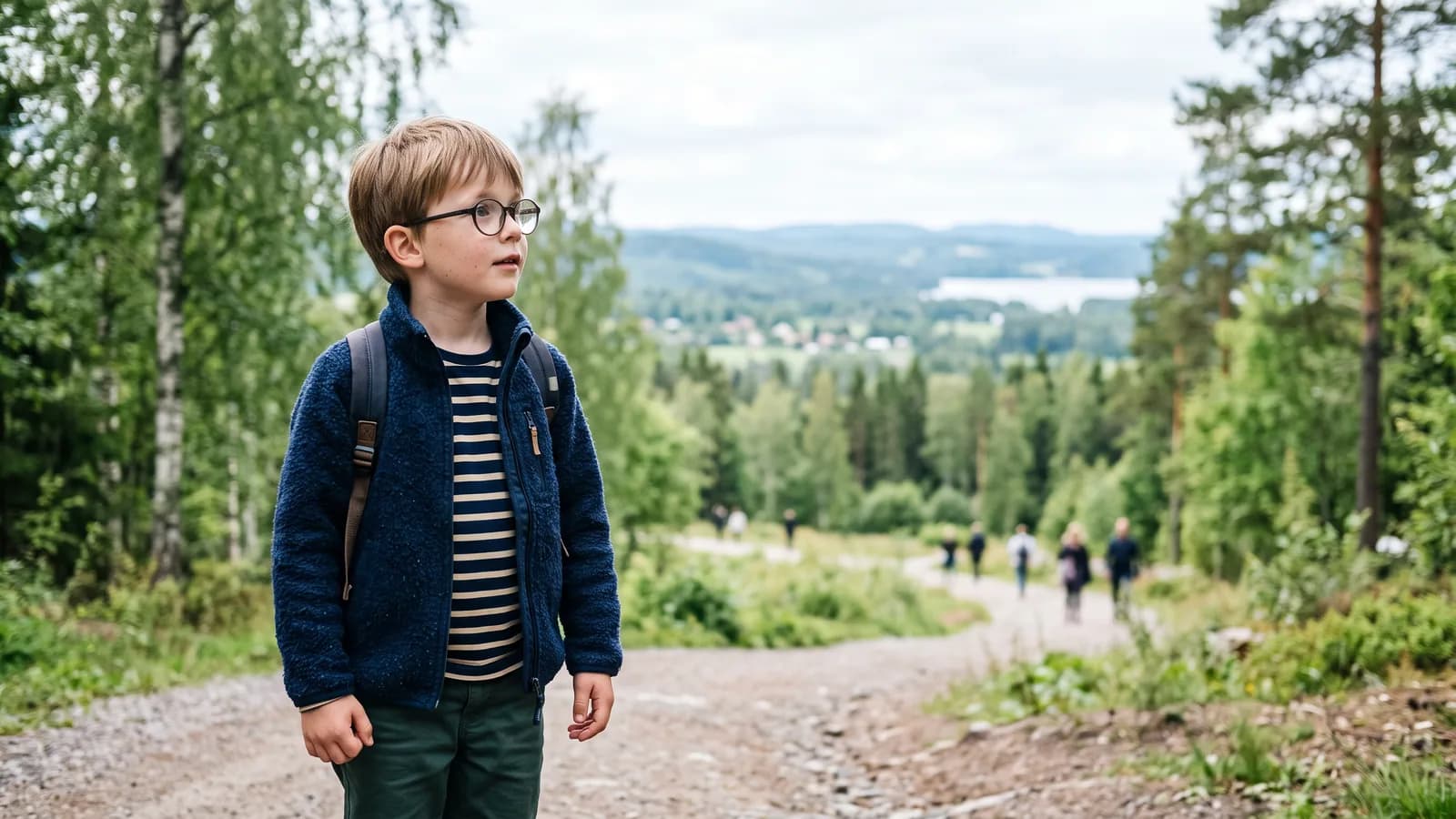 Et barn i skolealderen med briller står ude i et lyst nordisk parklandskab og kigger nysgerrigt mod horisonten