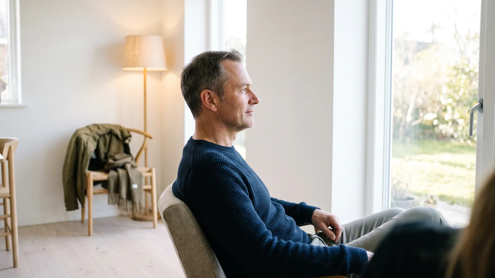En rolig mand i halvtredserne sidder afslappet ved et vindue og ser ud, uden bekymring