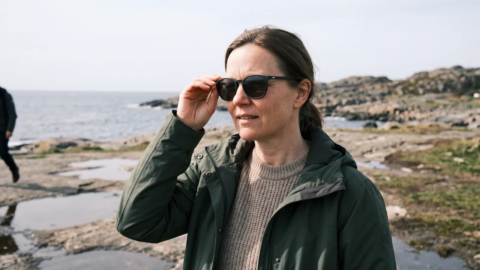 En kvinde i 40'erne tager solbriller med UV-filter på en solrig dag ved kysten, beskyttelse mod UV-stråler, der kan give pinguecula.
